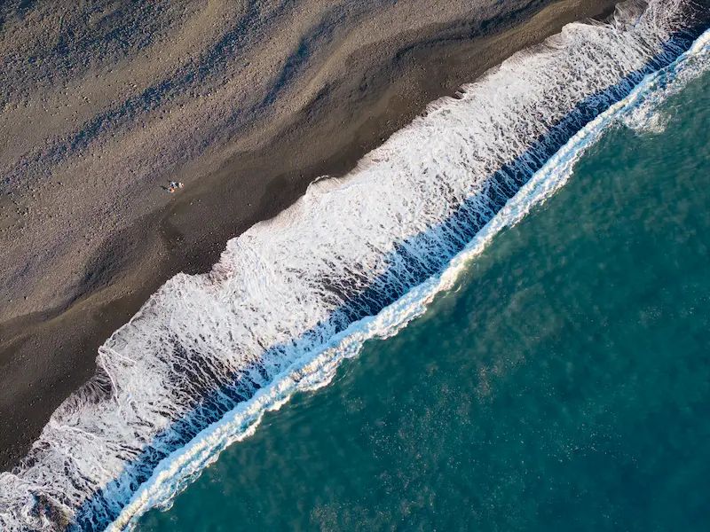 Vista aérea mostrando la espuma blanca de las olas turquesa rompiendo en la orilla de una playa de arena volcánica negra en La Palma, Canarias